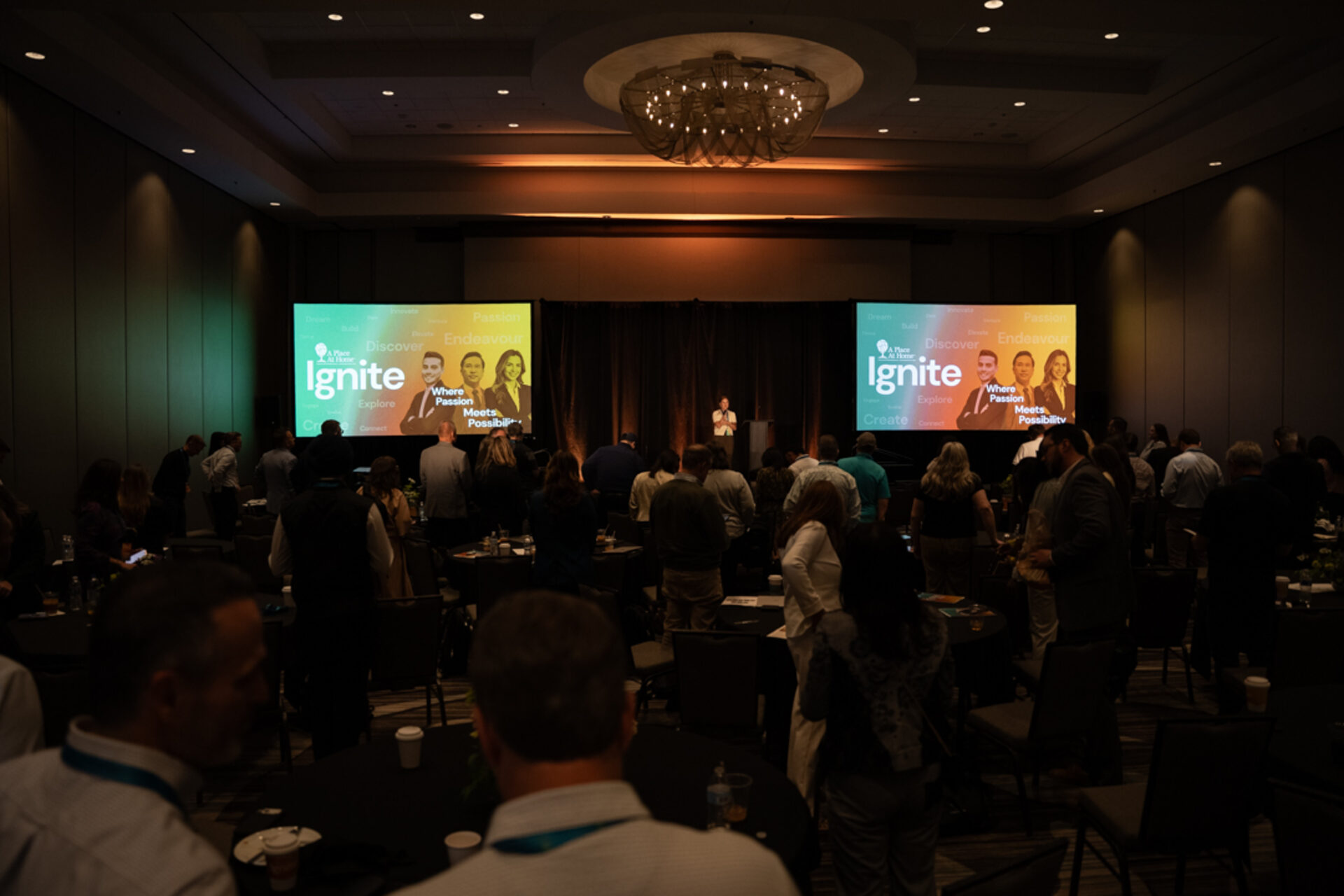 Attendees standing during an opening general session with dual widescreen content
